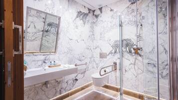 Un baño moderno con pared de mármol, cabina de ducha de vidrio, lavamanos blanco y puerta de madera.