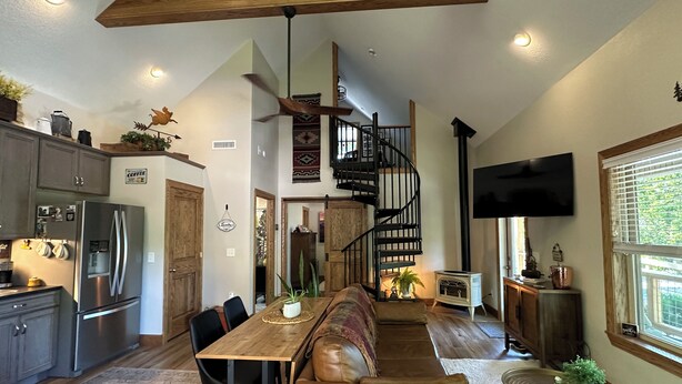 A spacious kitchen with a built-in refrigerator, a dining area with a wooden table and leather seating, a spiral staircase, and a large window with blinds.