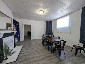 A dining area with a long wooden table and chairs, a fireplace, and a blue shelving unit. - 6BR Home | Sleeps 12+ | Fenced Yard + Pets Welcome (Evansville)