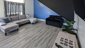 A modern living room with a sectional sofa, a black couch, a ceiling fan, and a large flat-screen TV mounted on the wall.