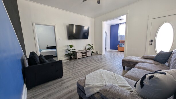 A modern living room with a flat-screen TV, a ceiling fan, and a large window.