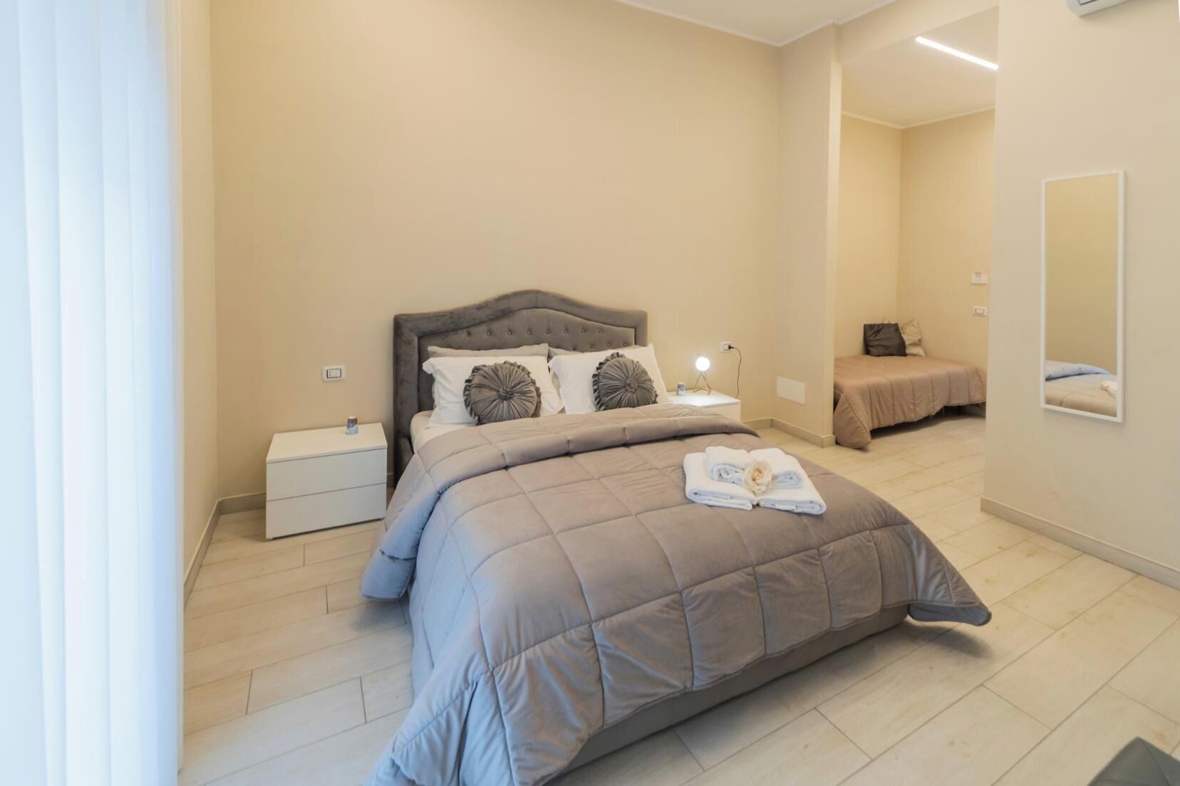 A modern bedroom with a large bed, a bedside table, a nightstand, and a mirror on the wall.