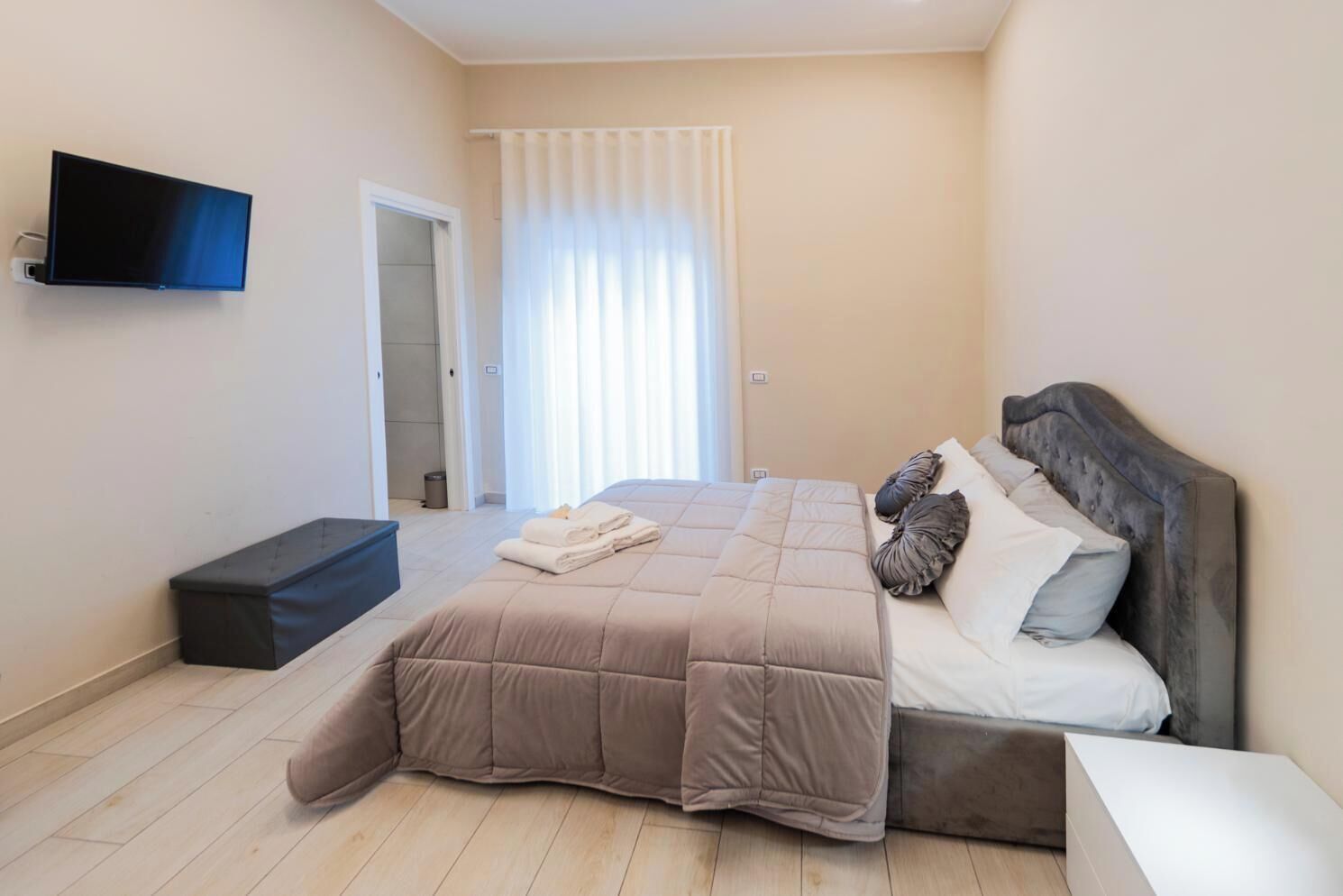 Un dormitorio con cama, televisión montada en la pared y ventana con cortinas.