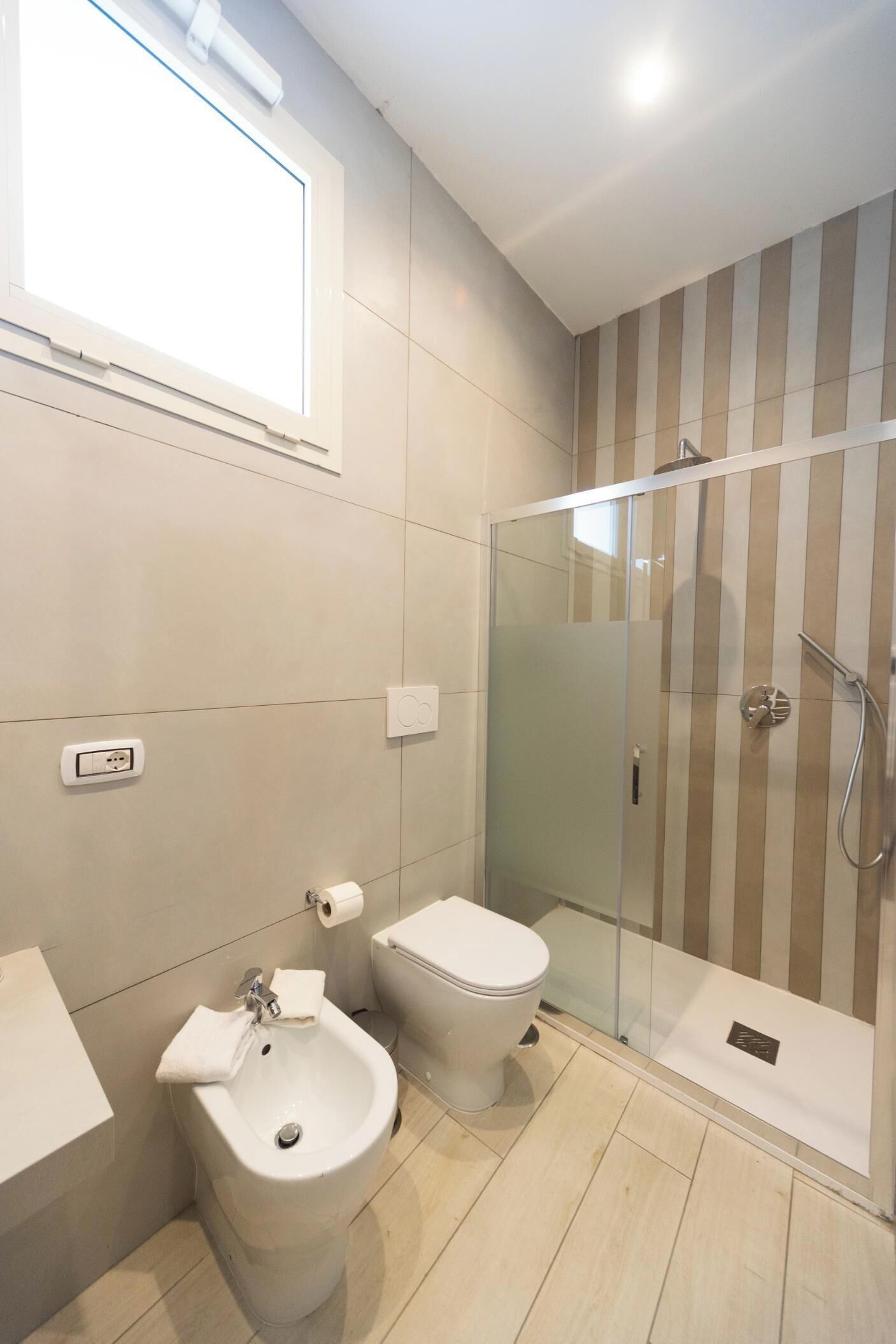 A modern bathroom with a glass-enclosed shower, a bidet, a toilet, and a sink.