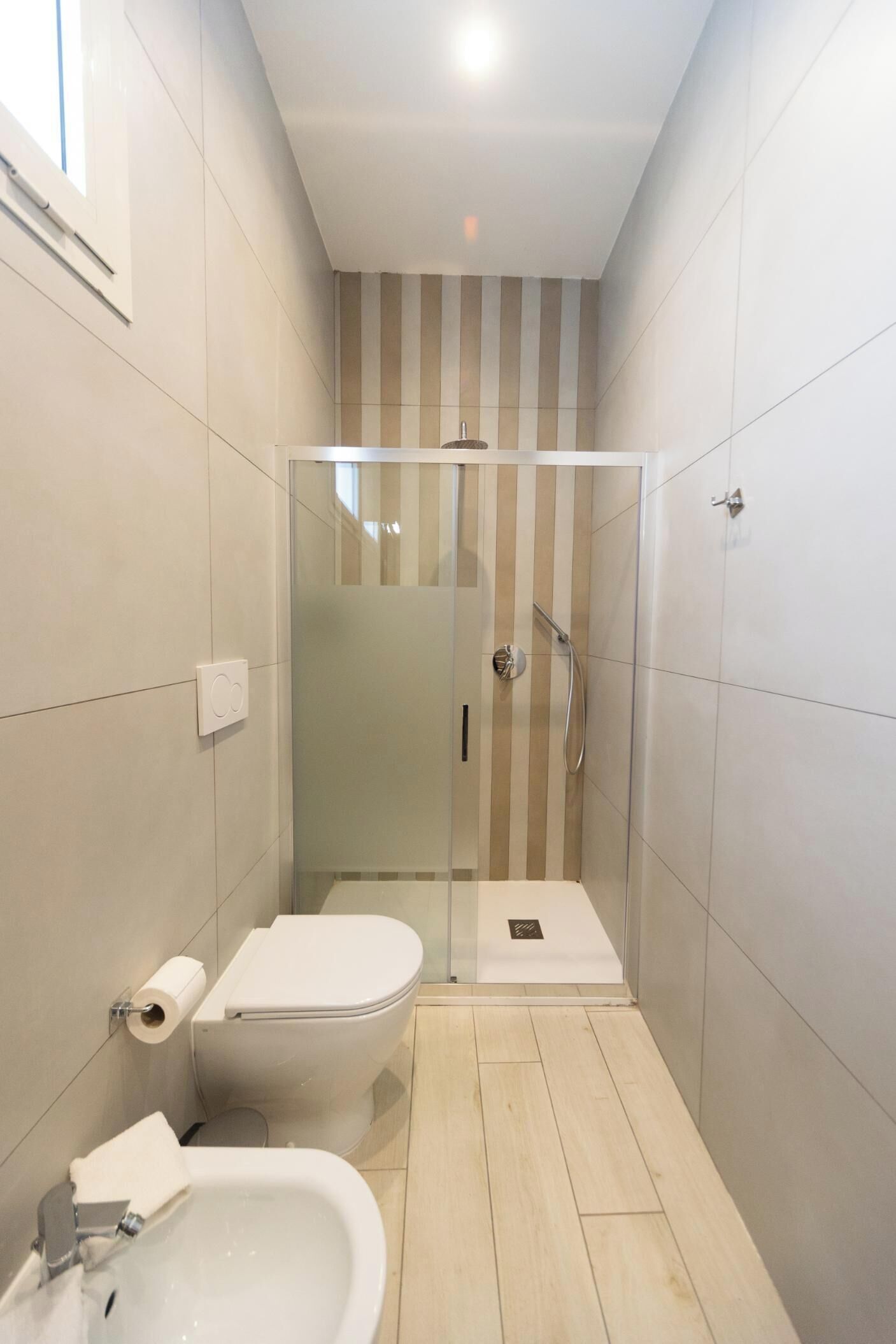 Ein schmales Badezimmer mit einer Duschkabine, einer Toilette und einem Waschbecken.
