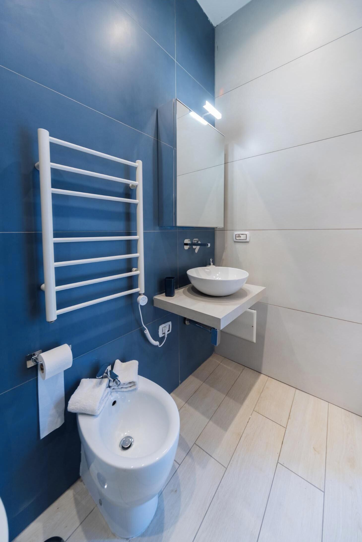 A modern bathroom with a blue wall, a white sink, a bidet, and a towel rack.