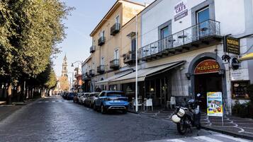 A street with parked cars and a motorcycle, buildings with balconies, and a sign for 'Mericano Restaurant'.