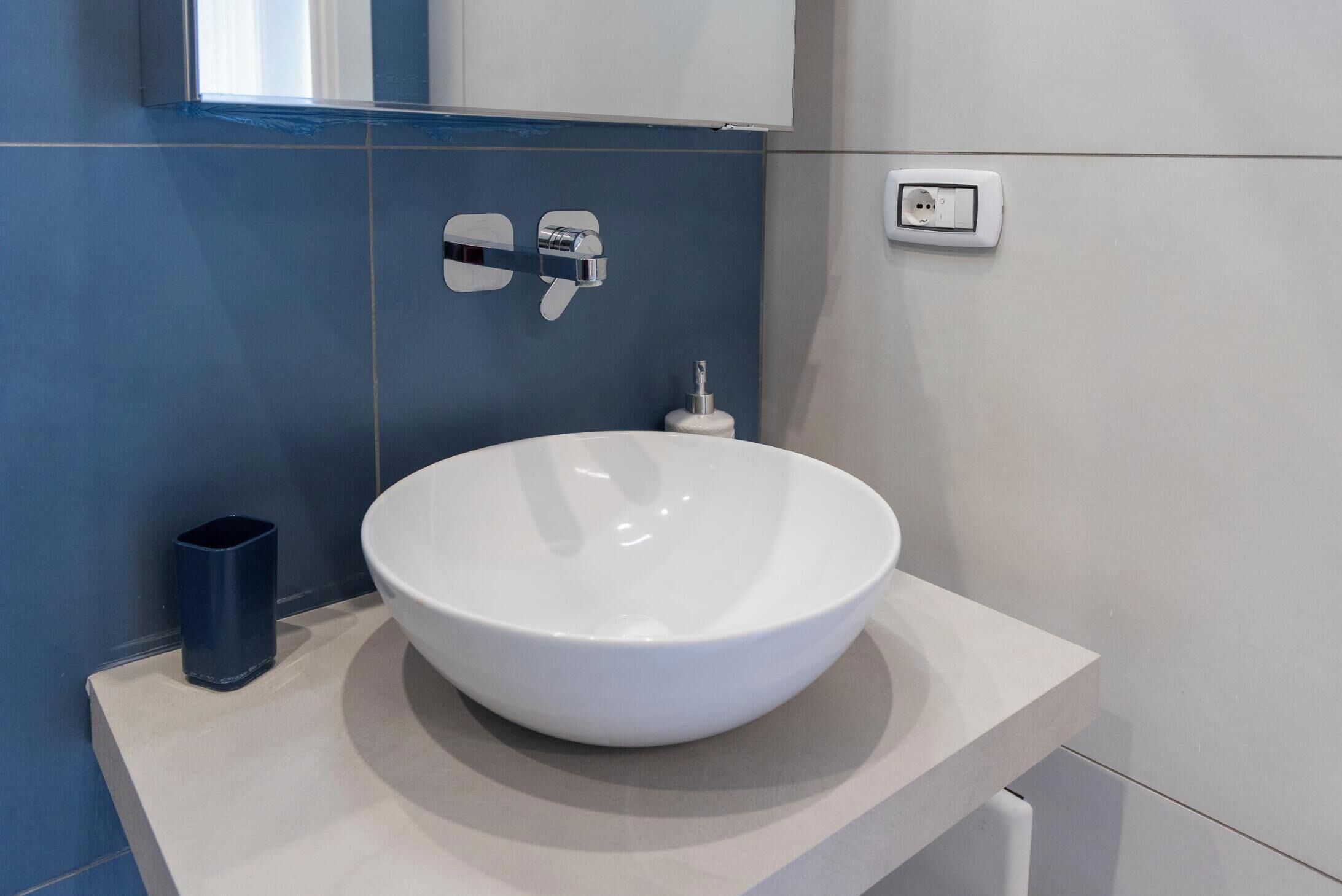 Une salle de bain moderne avec un grand lavabo blanc, un miroir au-dessus et un mur bleu.