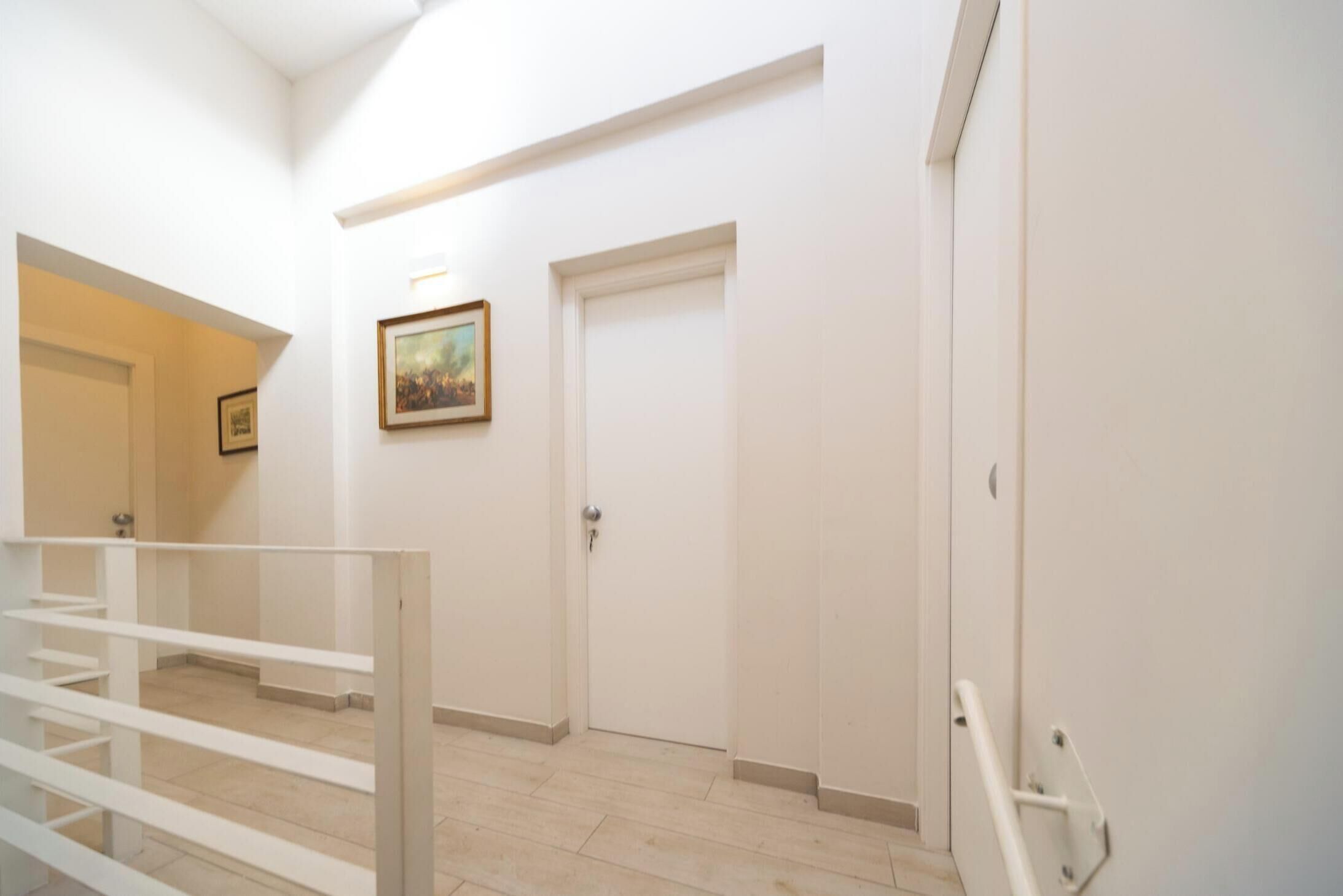 A hallway with white walls, a framed picture, and a closed door.