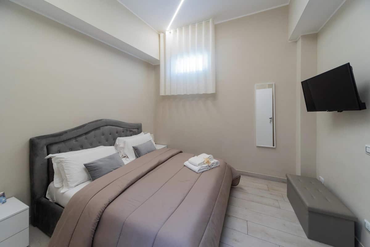 A bedroom with a bed, a nightstand, a TV, and a window with curtains.