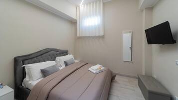 A bedroom with a bed, a nightstand, a TV, and a window with curtains.