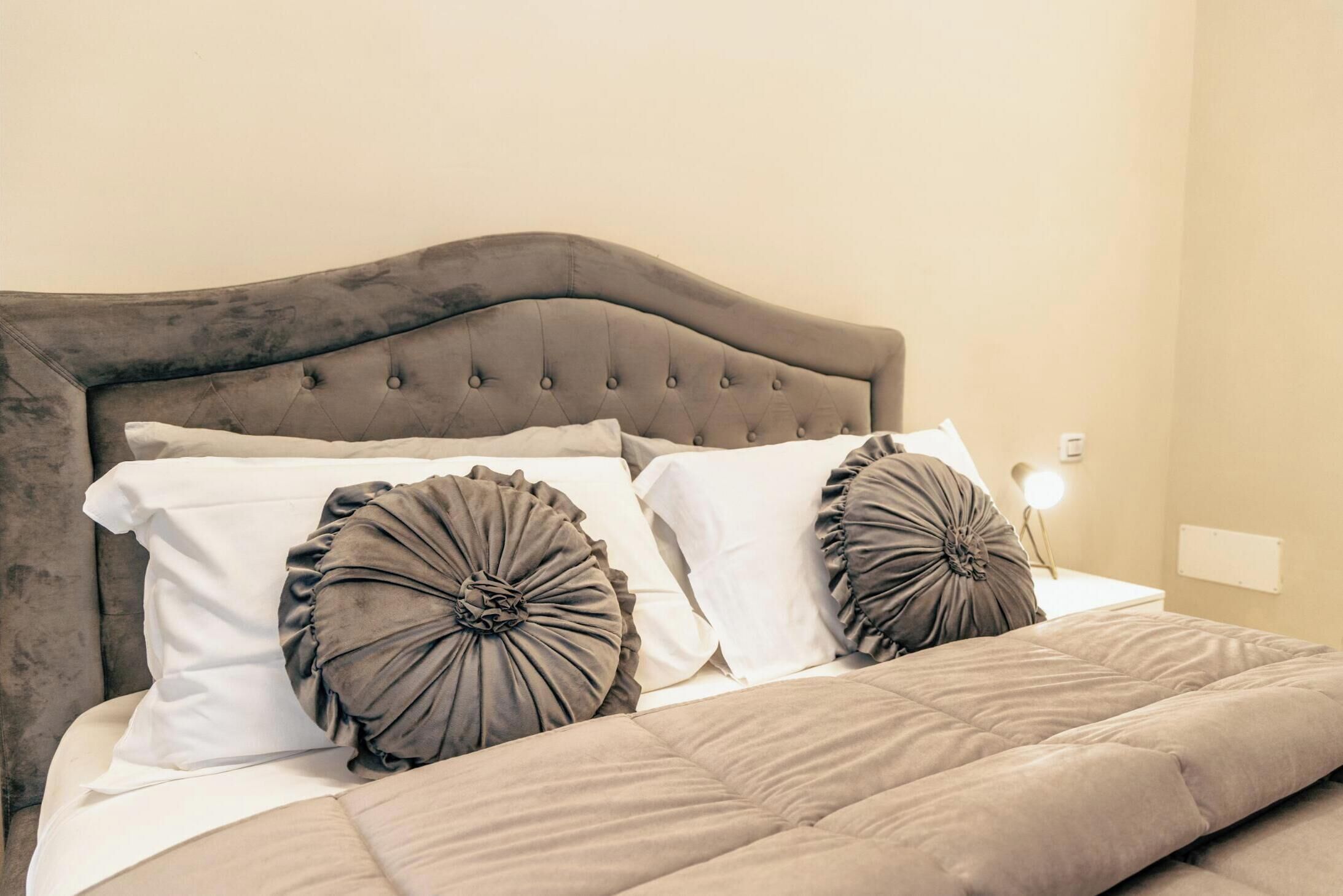 A bed with a tufted headboard, two pillows with ruffled designs, and a bedside lamp.