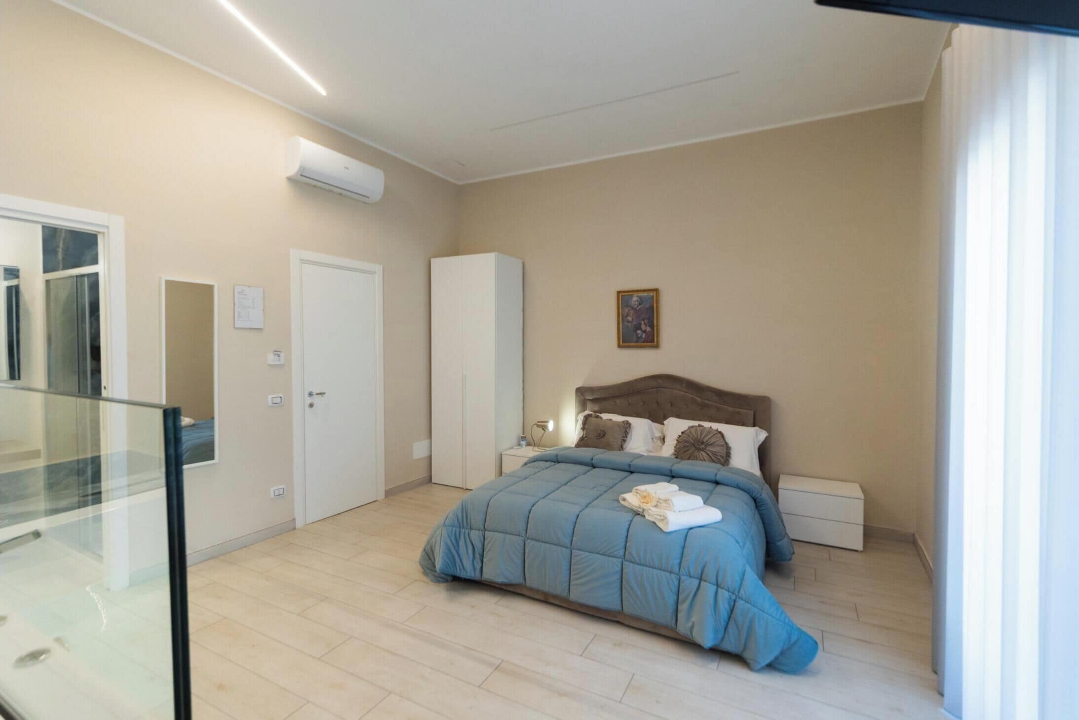 A bedroom with a bed, bedside tables, a wardrobe, and an air conditioning unit.