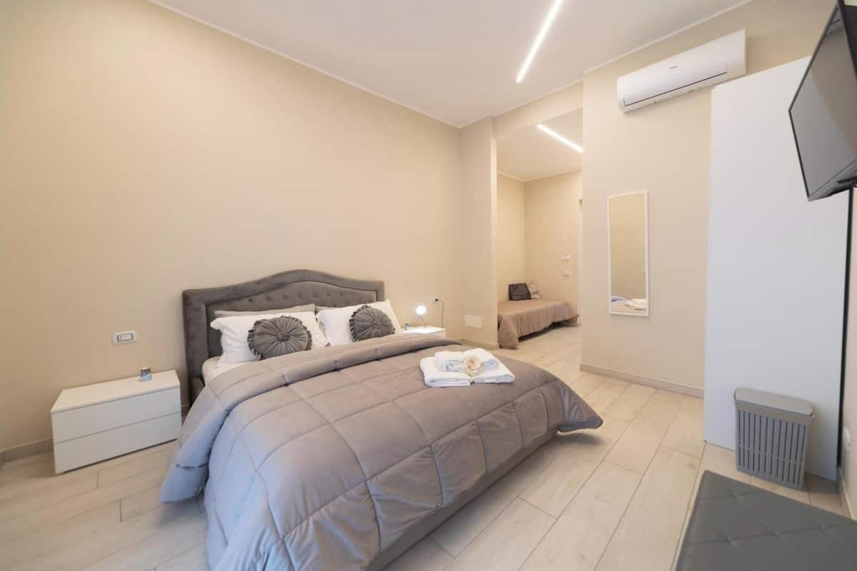 A modern bedroom with a large bed, bedside tables, a flat-screen TV, and a mirror.