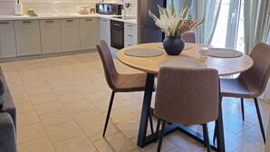 A modern kitchen with white cabinets, a built-in oven, and a refrigerator. There is a dining area with a round table and four chairs. - Tranquil 2BR Penthouse Petralona (Athina)