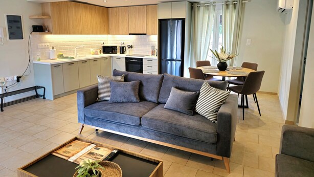 A modern living room with a grey sofa, a coffee table, and a dining area with a table and chairs. - Tranquil 2BR Penthouse Petralona (Athina)