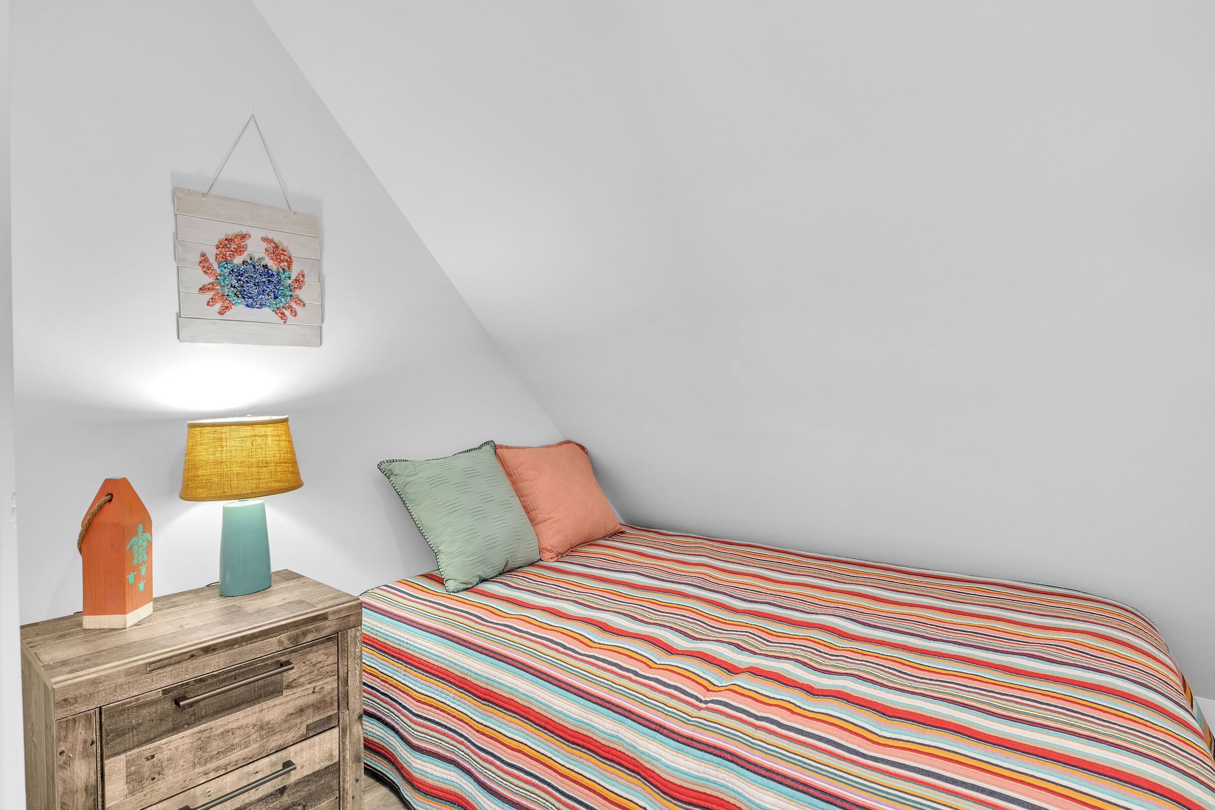 A bedroom with a bed, a nightstand, a lamp, and a wall hanging.