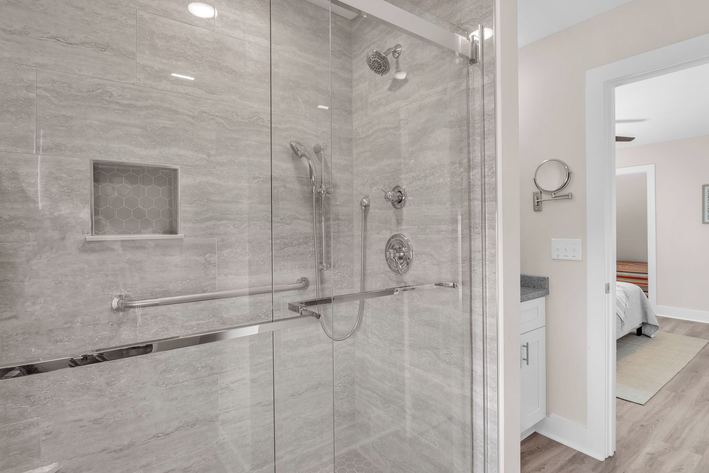 A modern bathroom with a glass-enclosed shower, a handrail, and a small hexagonal tile design on the wall.