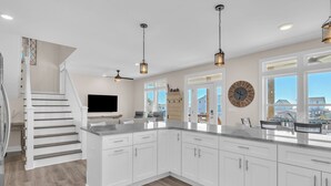 Una cocina moderna con gabinetes blancos, encimera de granito e iluminación colgante.