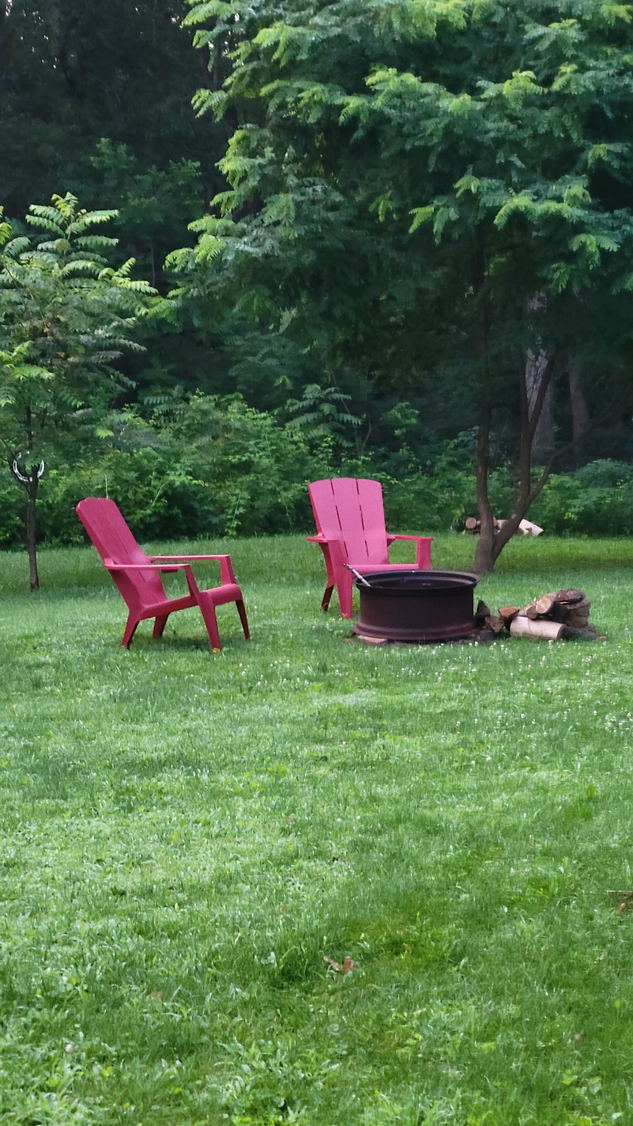 A grassy outdoor area with two red Adirondack chairs and a fire pit.