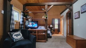 Un salon chaleureux avec un plafond en bois, un canapé en cuir noir, un téléviseur et une table basse sur laquelle se trouve un panier.