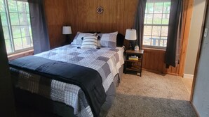 Une chambre à coucher aux murs lambrissés, avec un grand lit, deux tables de chevet dotées de lampes et une fenêtre avec des rideaux.