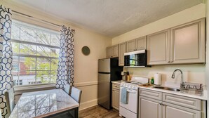 A kitchen with a dining table, cabinets, a refrigerator, a stove, and a microwave.