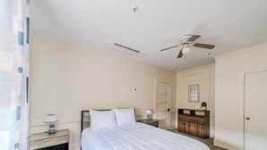 A bedroom with a bed, nightstands, a dresser, a ceiling fan, and a door.