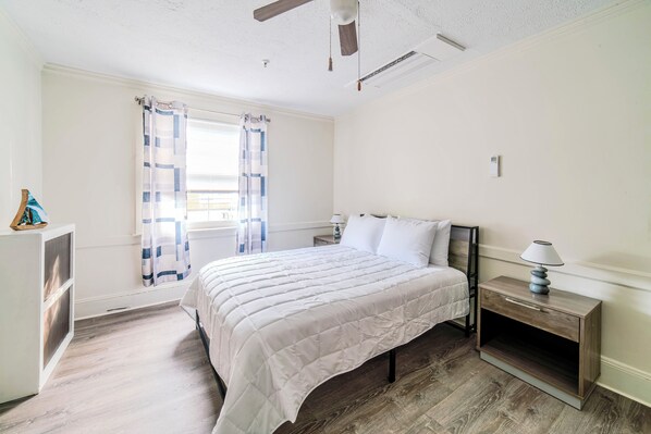 Un dormitorio con cama, mesita de noche y ventana con cortinas.
