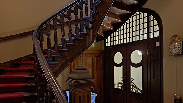 A grand staircase with wooden balusters, a white table with a white tablecloth, and a large arched doorway with glass panels.