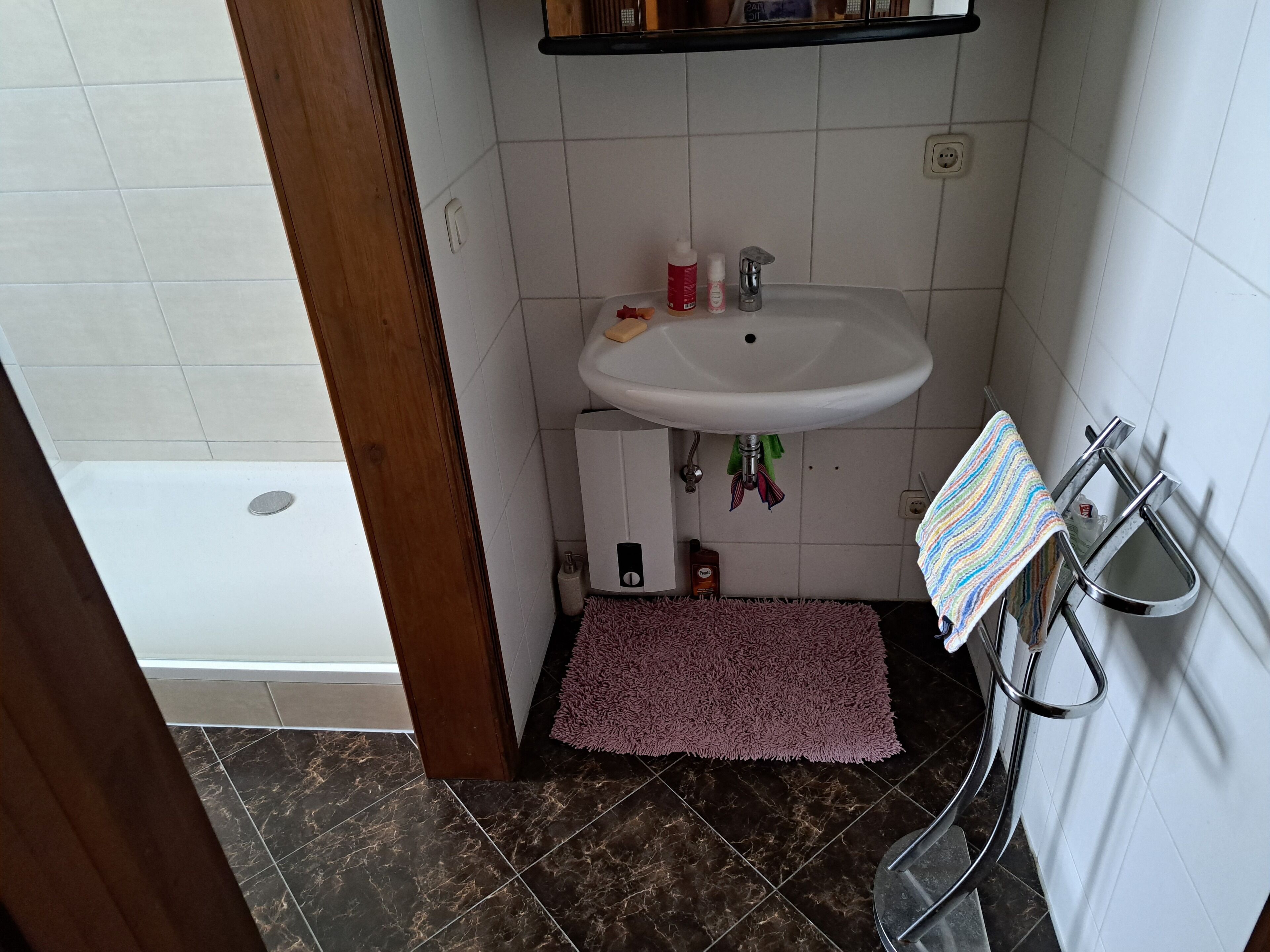 A bathroom with a white sink, a purple bath mat, and a striped towel hanging on a metal towel rack.