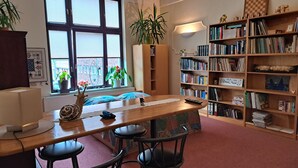 A cozy room with a wooden desk, two black chairs, a bookshelf, and a window with blinds.