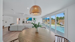 Amplia sala de estar con un gran ventanal con vistas a una piscina, una mesa de comedor de madera y un sofá blanco moderno.