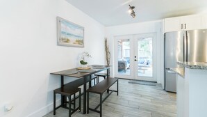 Una cocina con una mesa de madera y bancos, un refrigerador y una puerta que da a un espacio exterior.
