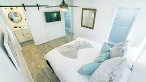 Un dormitorio con cama, televisor, espejo y ventilador de techo.