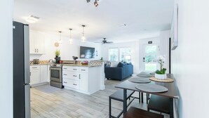 Una cocina moderna con armarios blancos, una isla central y un comedor con una mesa y un banco de madera.