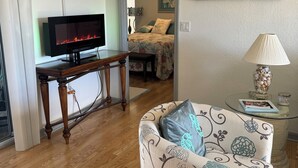 A living room with a flat-screen TV, a sofa, a coffee table, and a painting on the wall. - Heated pool home. Desirable 3-bedroom located in CapeCoral loads of extras! (Cape Coral)