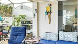 A patio area with a blue sofa, a metal table, and a parrot decoration. - Heated pool home. Desirable 3-bedroom located in CapeCoral loads of extras! (Cape Coral)