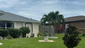A well-maintained lawn with a palm tree, a small bush, and a decorative stone planter. - Heated pool home. Desirable 3-bedroom located in CapeCoral loads of extras! (Cape Coral)