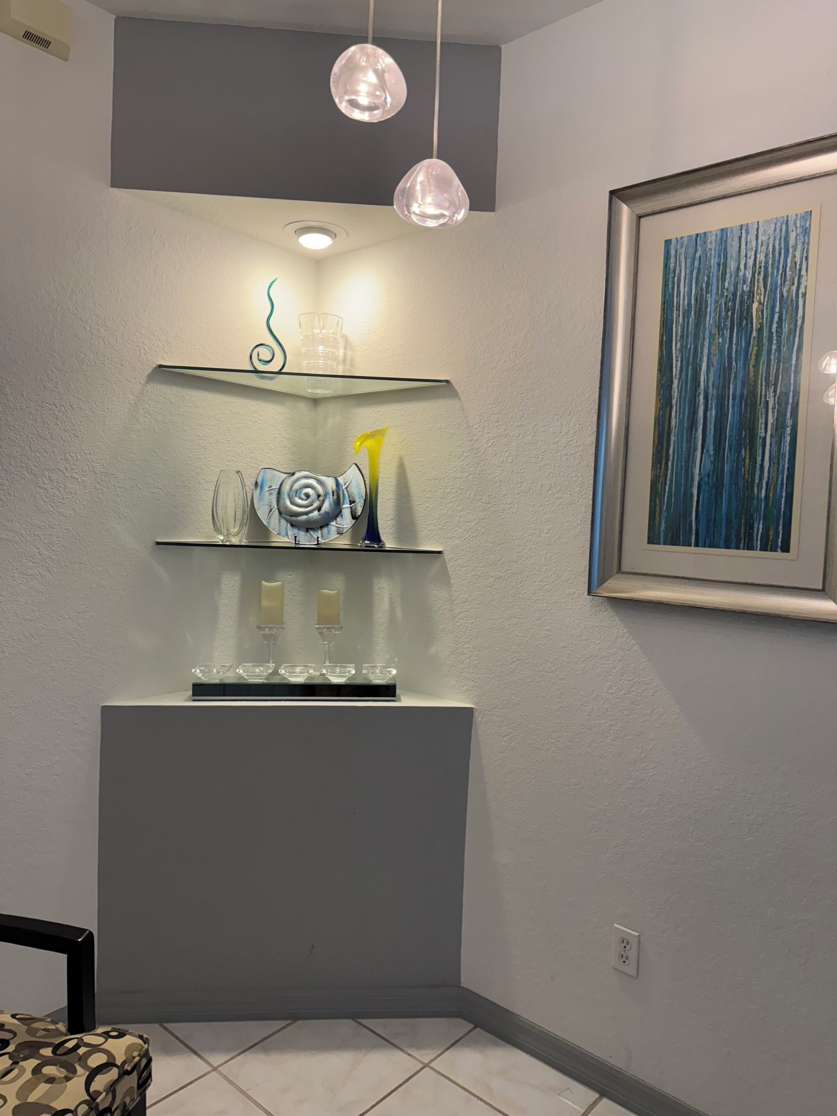 Habitación de esquina con un expositor de vidrio, un cuadro abstracto enmarcado y una silla.
