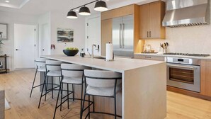 A modern kitchen with a central island, bar stools, stainless steel appliances, and pendant lighting. - Frontgate 228 - 3 Bedroom Residence (Avon)