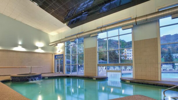 An indoor swimming pool with clear windows, a hot tub, and a view of the outside. - Available February 17-21 2025. Sleep 8 - 2-bed apt on Jiminy Peak.  Ski in/out! (Hancock)