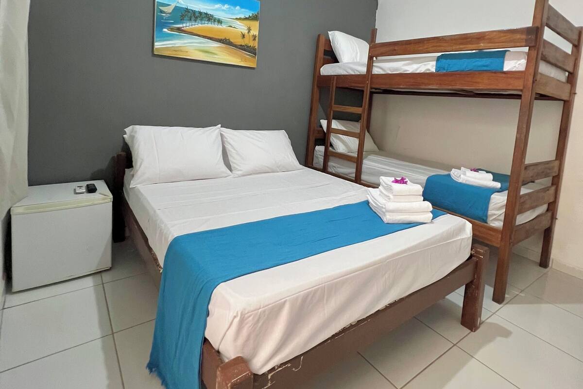 Un dormitorio con una cama litera, una cama individual, un pequeño armario blanco y un cuadro de una playa.