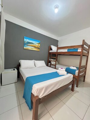 A bedroom with a bunk bed, a single bed, a small white cabinet, and a painting of a beach scene. - Pousada Vila do Sol (Jijoca de Jericoacoara)