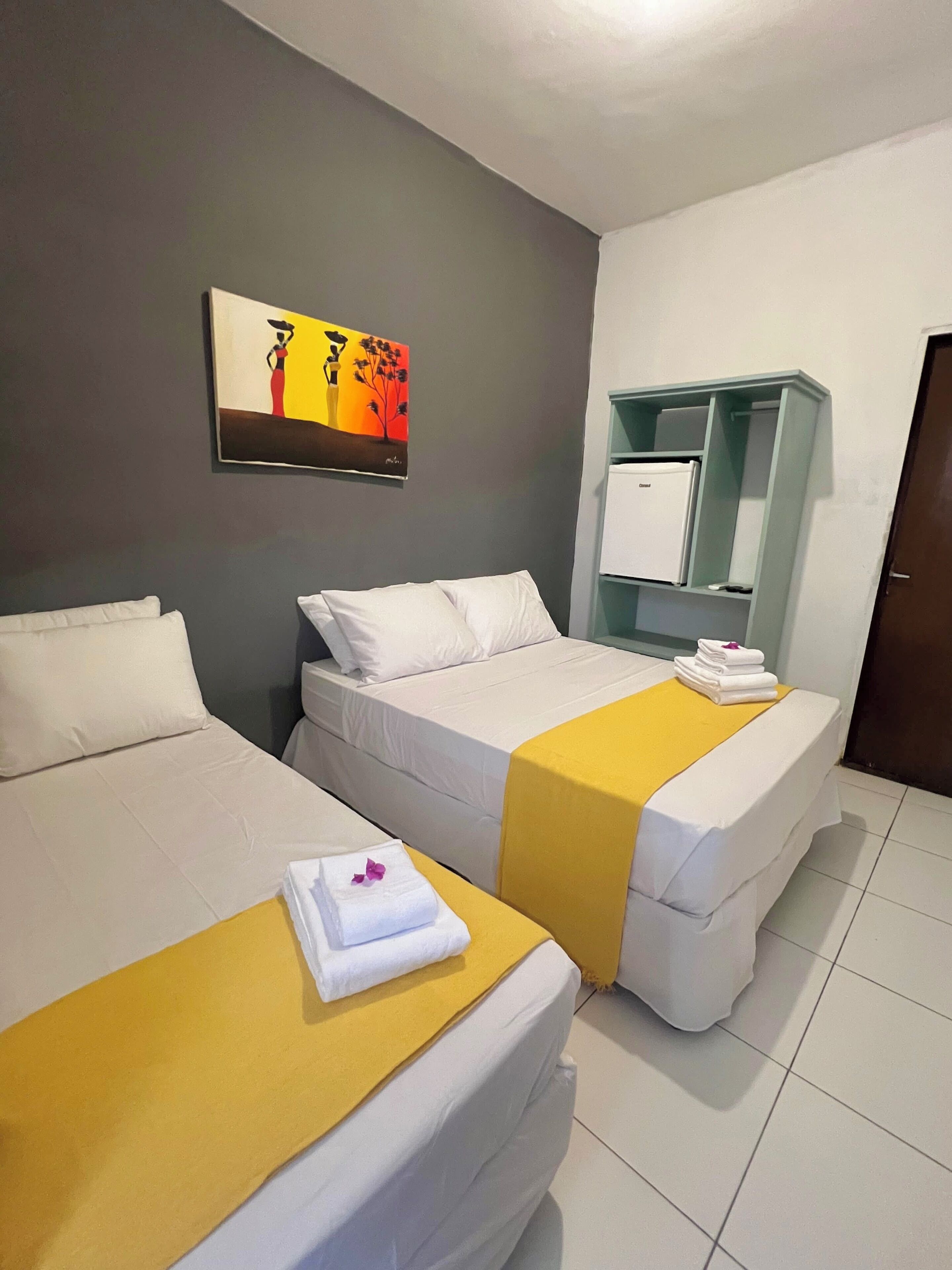 Una habitación de hotel con dos camas, un cuadro en la pared, un minibar y una puerta.