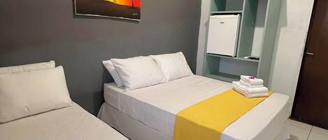 A hotel room with two beds, a painting on the wall, a minibar, and a door.