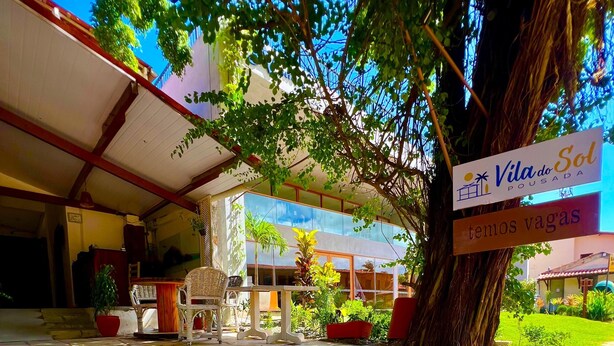 A covered outdoor area with stone steps leading to a building entrance, surrounded by potted plants and a large tree.