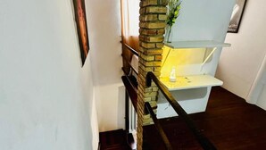 A staircase with a wooden handrail, a stone pillar, and a white bench with a vase of flowers.