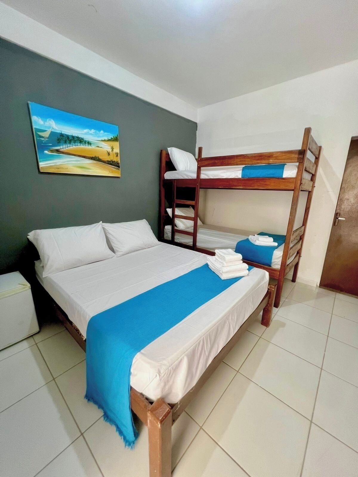 A room with a single bed, a bunk bed, and a painting of a beach scene.