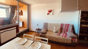 A cozy living area with a sofa, dining table, and a kitchen area with cabinets and a refrigerator. - Apartment facing the mountains -la Belle étoile (Eyne)